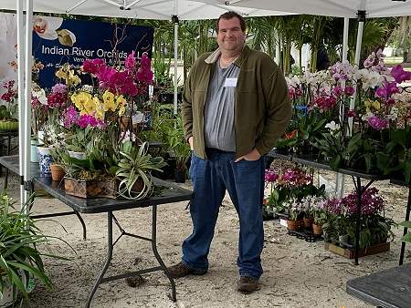 Man standing next to a table with yellow and pink orchids